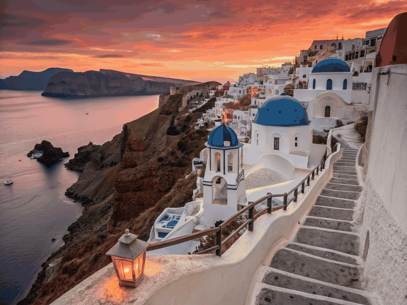 Whitewashed cliffside buildings and blue domes of Oia overlooking the caldera at sunset
