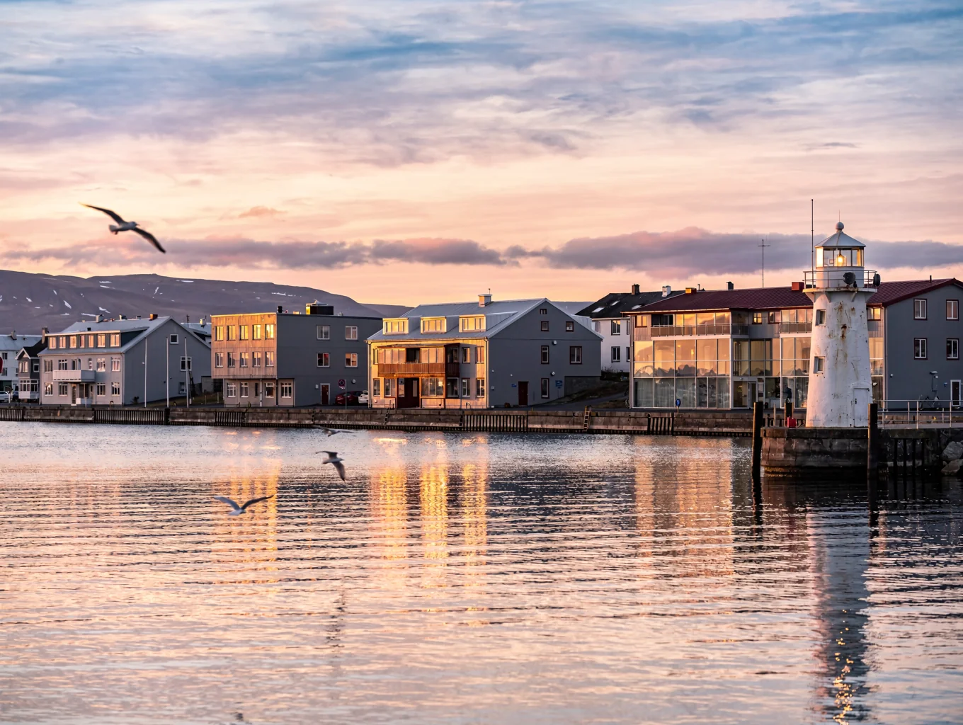 Vibrant painted rooftops and fishing boats moored in the historic harbor of Reykjavik against mountain vistas
