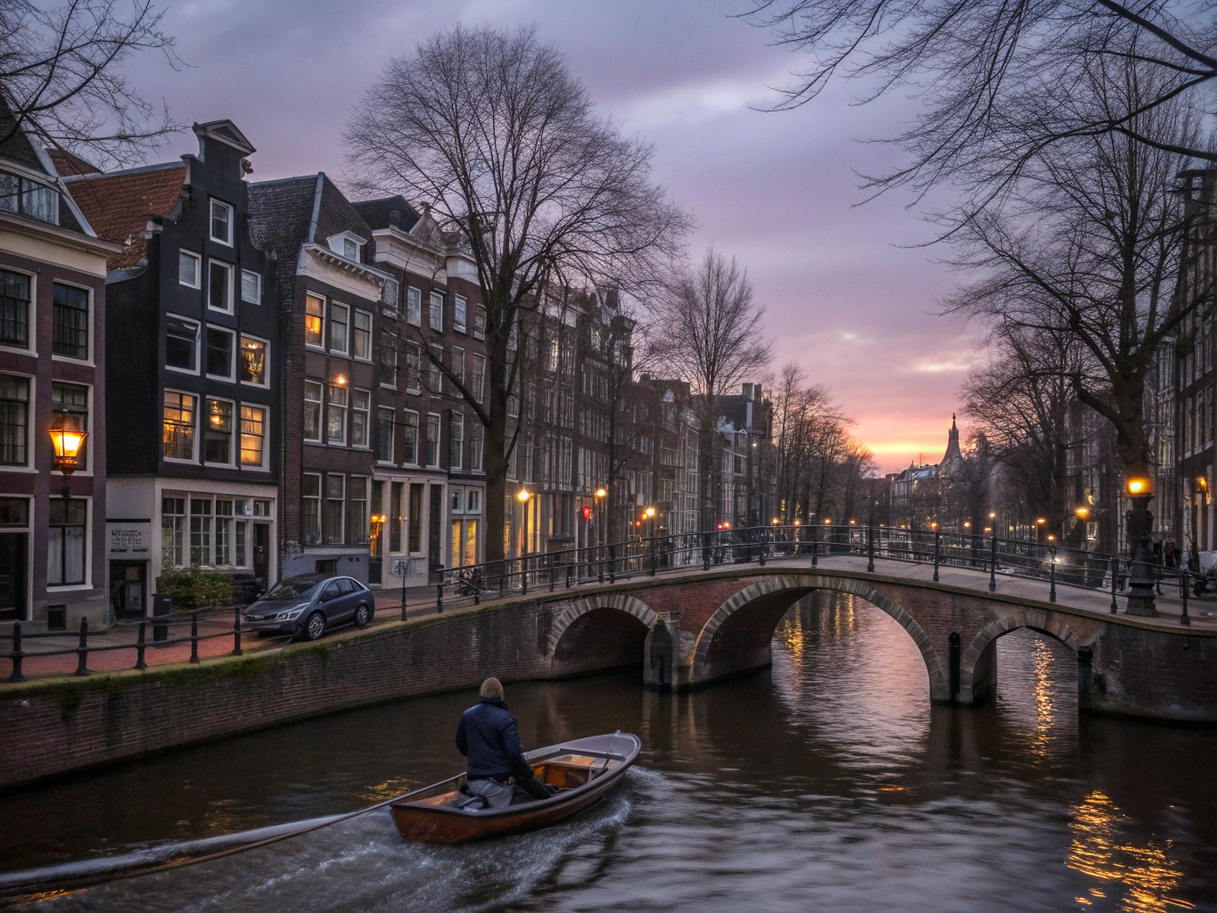 Bicycles resting along an arched brick canal bridge at dusk in Amsterdam