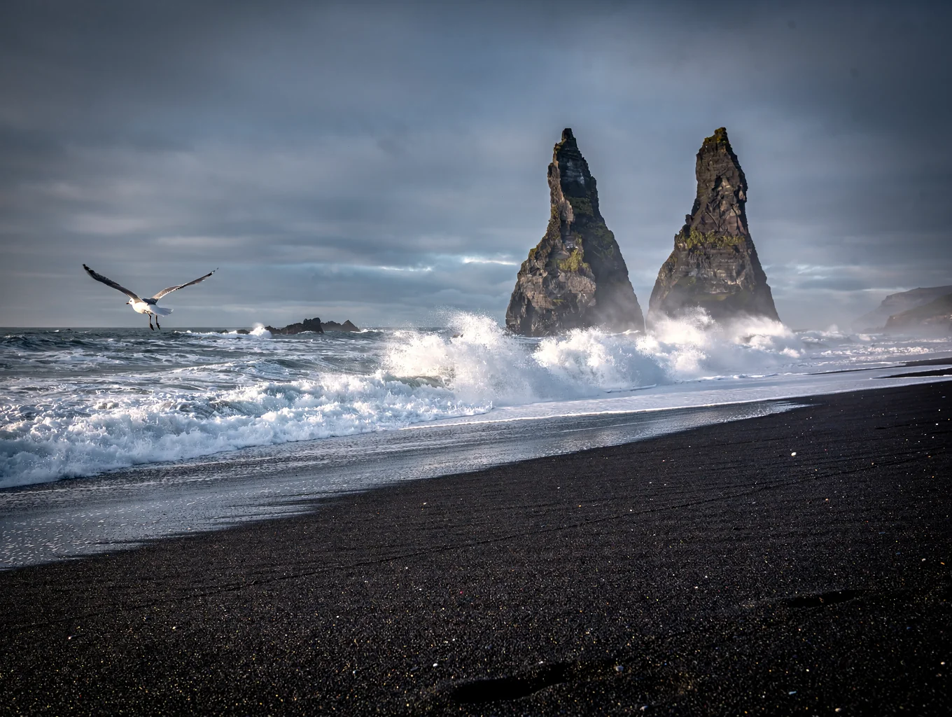 Basalt column cliffs and breaking ocean swells on dark volcanic sand
