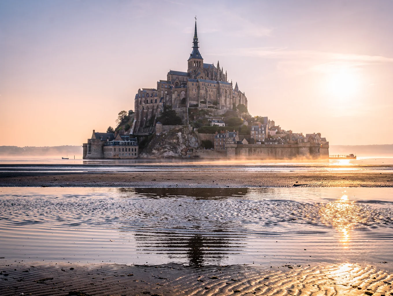 Silhouetted abbey of Mont-Saint-Michel surrounded by mirror-like tidal sand