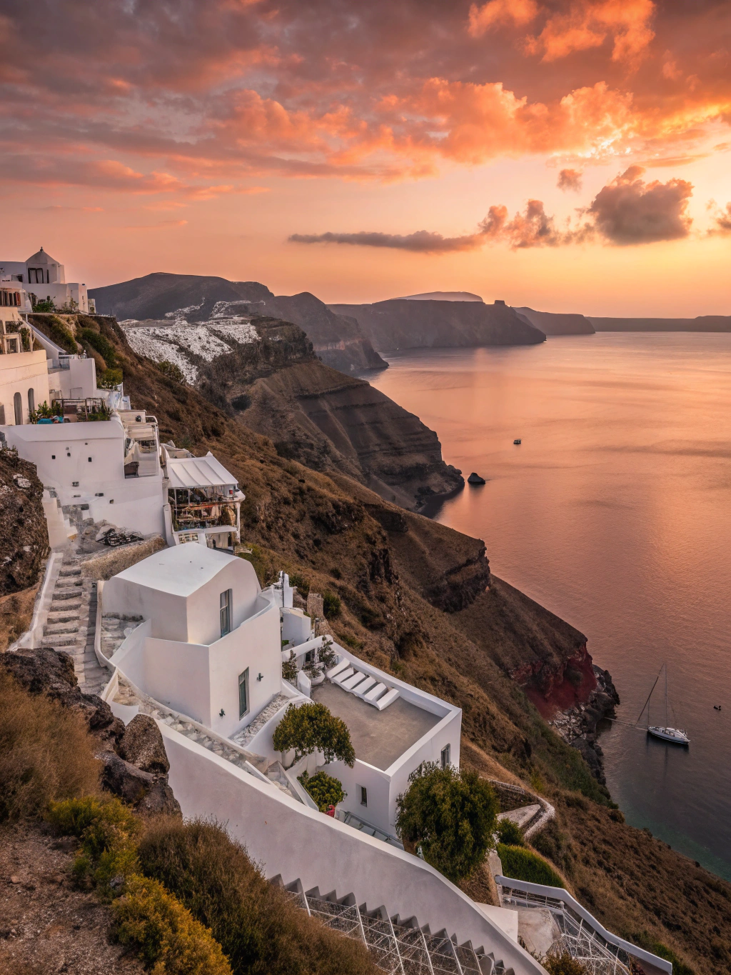 White tiered Cycladic cliff terraces overlooking the deep blue caldera under a golden sunset in Santorini
