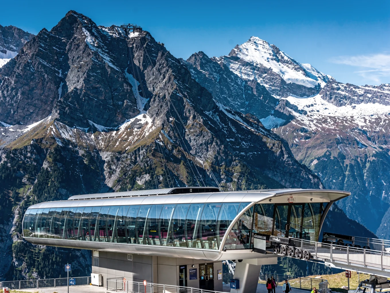Modern curved glass cable car station set against rugged snow-capped alpine peaks